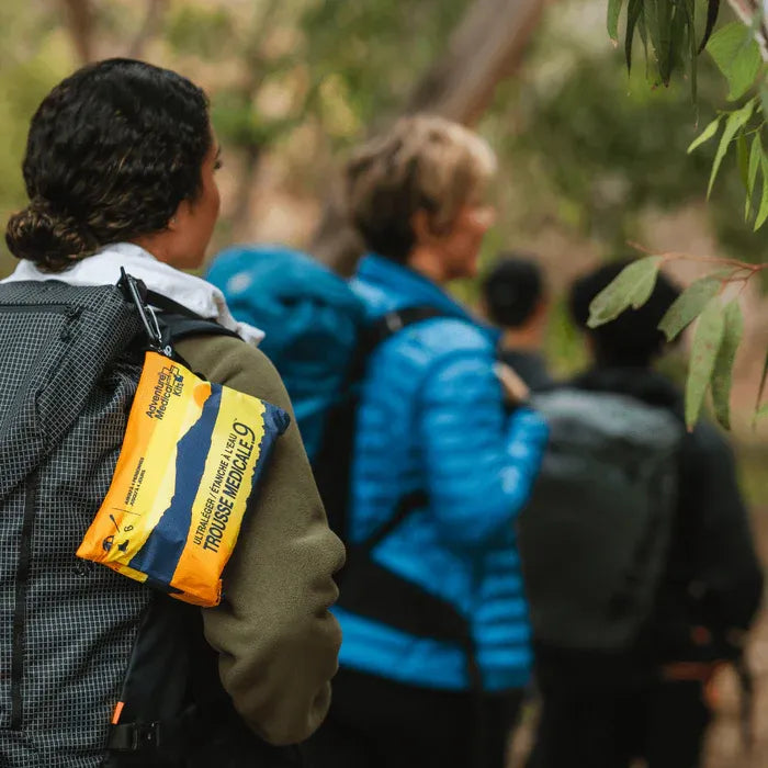 Person with a backpack and a visible Adventure Medical Kits first aid kit in a forest setting