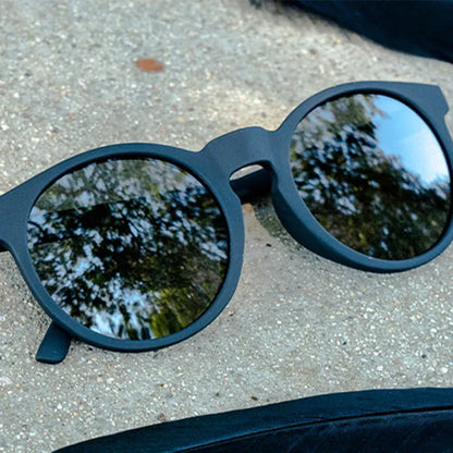 Black round goodr sunglasses with reflective lenses on a concrete surface