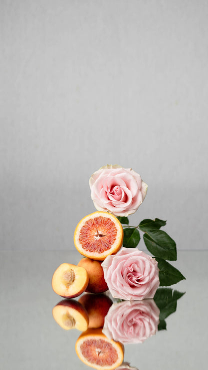 Pink roses and blood oranges on a reflective surface with a gray background