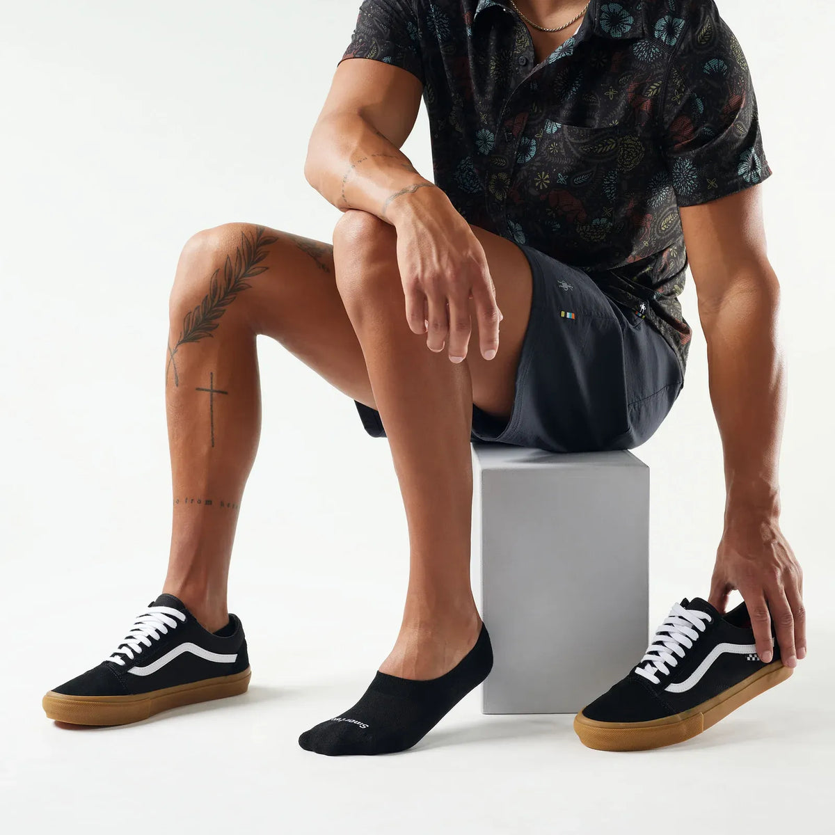 Person wearing black sneakers nad black Smartwool No Show Socks with white laces on a plain background