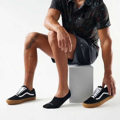 Person wearing black sneakers nad black Smartwool No Show Socks with white laces on a plain background