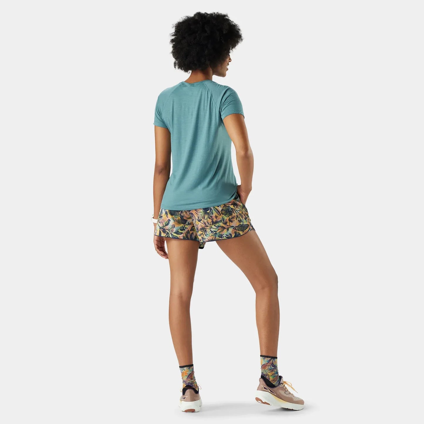 Woman wearing a Smartwool Active Ultralite teal t-shirt and patterned shorts on a white background