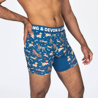 A man wearing blue boxer briefs with a playful dog print and a solid blue inner leg panel. The waistband features white text reading 'DEVON & LANG'.
